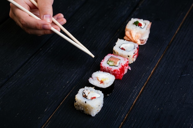 Vrouwelijke hand neemt eetstokjes sushi rolt met Chinese eetstokjes. Liggend op een zwarte houten plank. Uitzicht van boven.