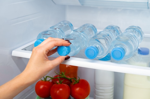 Vrouwelijke hand nemen fles water uit een koelkast close-up