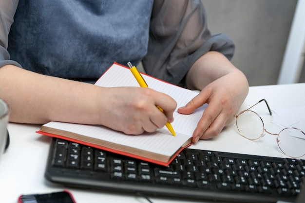 Vrouwelijke hand schrijft in notitieblok op de werkplek. Taakbeheer. Taken plannen. Boekhoudster aan het werk.