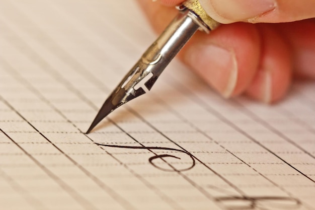 Foto vrouwelijke hand schrijft met de inktzwarte pen op een vel wit papier met strepen briefpapier op bureau close-up bovenaanzicht spellinglessen en kalligrafie oefeningen sjabloon lay-out achtergrondmacro