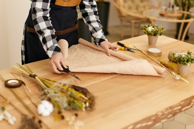 Vrouwelijke hand snijden ambachtelijk papier op houten tafel. Studio voor bloemsierkunst