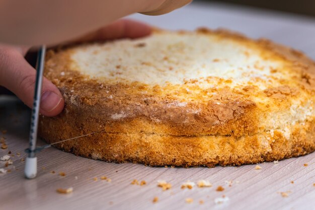 Foto vrouwelijke hand snijdt spons cheesecake met kokosnoot op een houten tafel