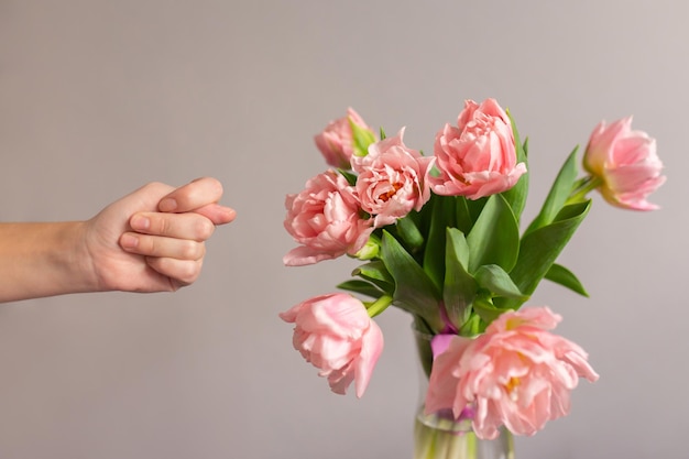 Vrouwelijke hand toont een vijgengebaar Boeket roze tulpen in een glazen vaas Humor concept