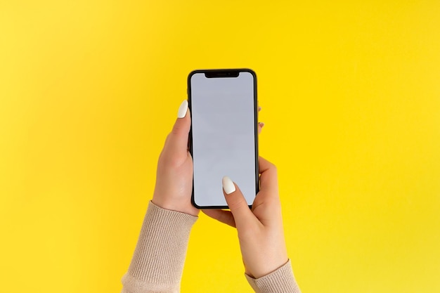 Vrouwelijke hand vasthouden en aanraken op mobiele smartphone met wit scherm Geïsoleerd op geel Fotosjabloon voor alle afbeeldingen op het display van de mobiele telefoon Lay-out met gemakkelijk verwijderbare telefoonmonitorachtergrond