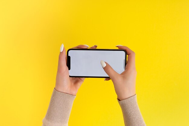Vrouwelijke hand vasthouden en aanraken op mobiele smartphone met wit scherm Geïsoleerd op geel Fotosjabloon voor alle afbeeldingen op het display van de mobiele telefoon Lay-out met gemakkelijk verwijderbare telefoonmonitorachtergrond