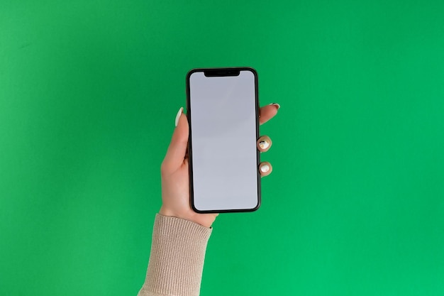 Vrouwelijke hand vasthouden en aanraken op mobiele smartphone met wit scherm Geïsoleerd op groen Fotosjabloon voor afbeeldingen op het display van de mobiele telefoon Lay-out met gemakkelijk verwijderbare telefoonmonitorachtergrond
