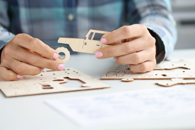 Vrouwelijke handen assembleren houten speelgoedauto uit verschillende delen. Ambachten van bomen concept