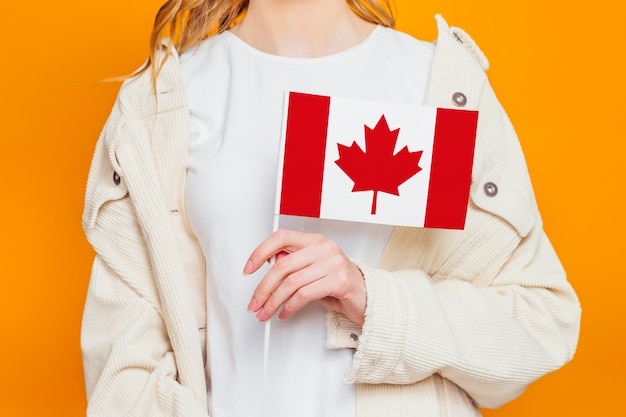 Vrouwelijke handen die de vlag van Canada houden die over oranje achtergrond wordt geïsoleerd