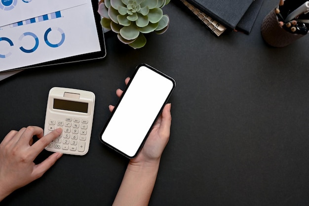 Vrouwelijke handen die een rekenmachine gebruiken en een mockup van een smartphone boven de werkruimte houden