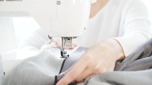 Vrouwelijke handen die grijze doek op een witte naaimachineclose-up naaien