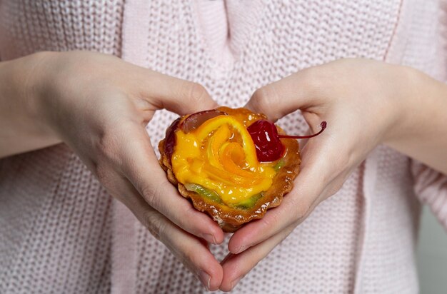 Vrouwelijke handen die lekkere cupcake met bessen en sinaasappel vasthouden en hartvorm maken. Close-up shot