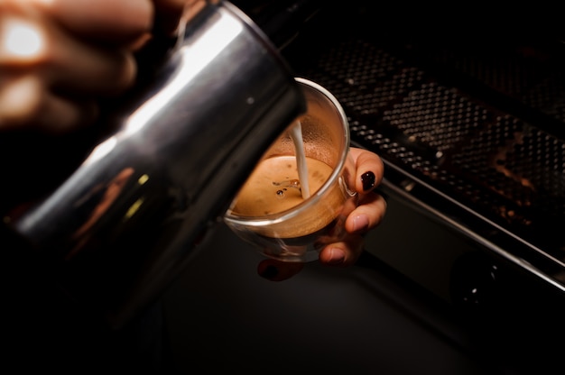 Vrouwelijke handen die melk van waterkruik gieten in de koffiekop