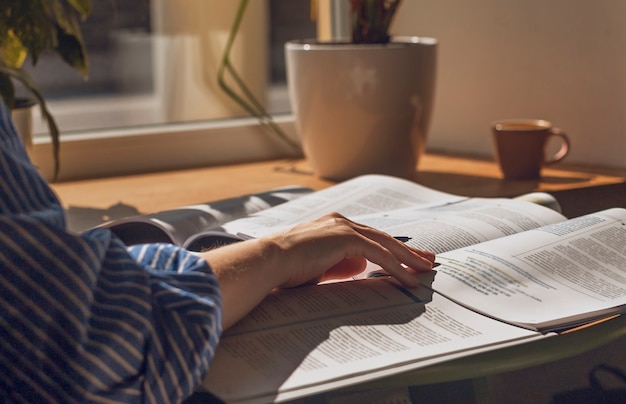 Vrouwelijke handen die met pen in notitieboekje schrijven die aantekeningen maken die met academisch leerboek van dichtbij studeren