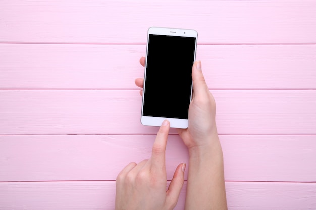 Vrouwelijke handen die mobiele telefoon met het lege scherm op roze houten achtergrond houden. smartphone op houten tafel.