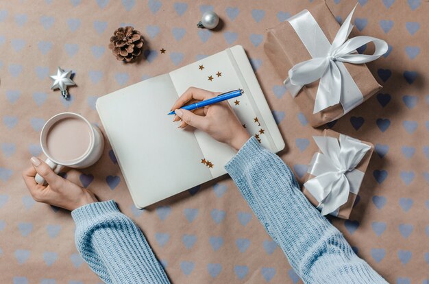 Vrouwelijke handen die wenslijst binnen schrijven aan notitieboekje dichtbij giften