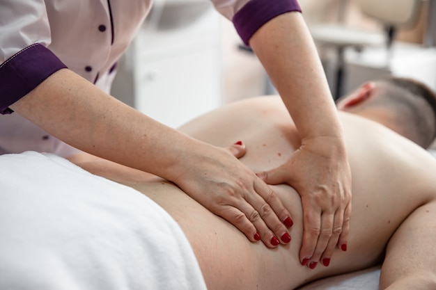 Vrouwelijke handen doen een rugmassage aan een man in de salon.