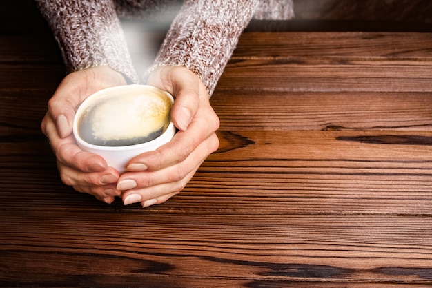 Vrouwelijke handen en koffie op houten achtergrond