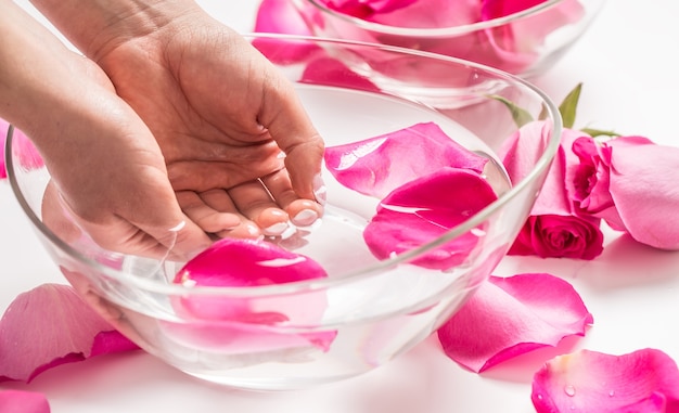 Vrouwelijke handen en kom spa-water met roze rozen en bloemblaadjes.