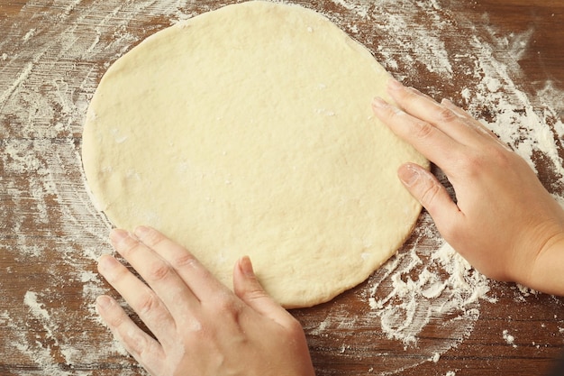 Vrouwelijke handen en uitgerold deeg op keukentafel close-up