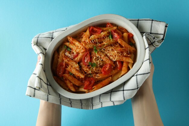 Vrouwelijke handen houden dienblad met pasta met tomatensaus op blauwe geïsoleerde achtergrond