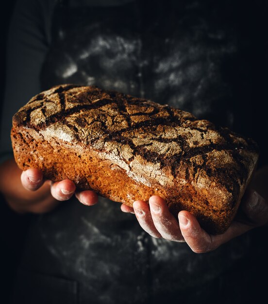 Vrouwelijke handen houden donker roggebrood vast.