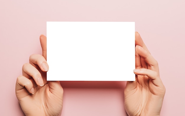 Vrouwelijke handen houden een blanco vel papier op een roze achtergrond. Advertentie ruimte