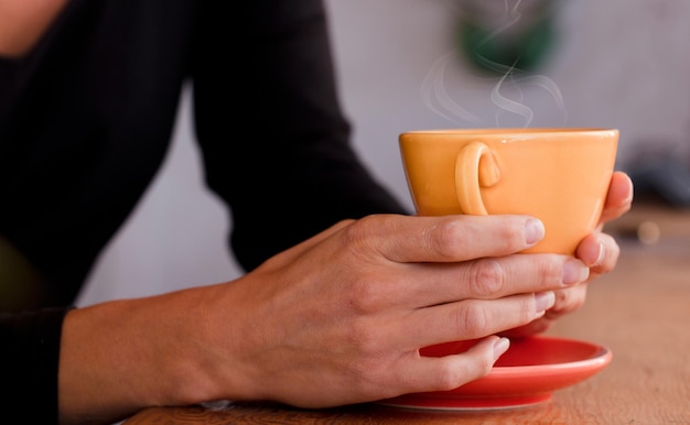 Vrouwelijke handen houden een gele kop met koffie vast Focus op de kop