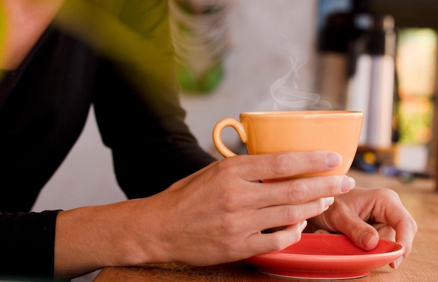 Vrouwelijke handen houden een gele kop met koffie vast Focus op de kop