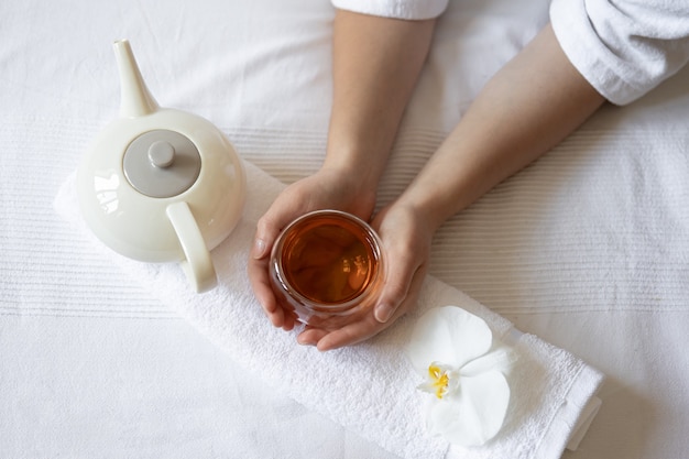 Vrouwelijke handen houden een kopje thee, een orchideebloem en een theepot vast, het concept van spabehandelingen en ontspanning.