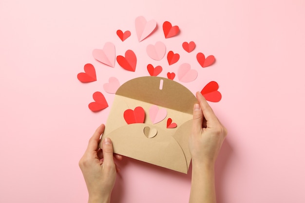 Vrouwelijke handen houden envelop op roze achtergrond met decoratieve harten