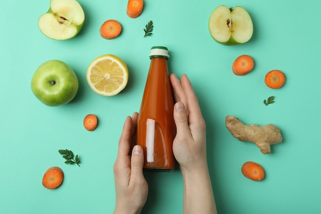 Vrouwelijke handen houden fles wortelsap op munt geïsoleerde achtergrond met ingrediënten
