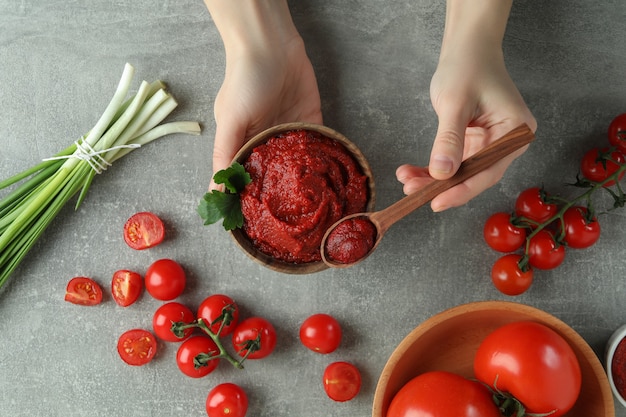 Vrouwelijke handen houden kom en lepel met tomatenpuree op grijze achtergrond met ingrediënten