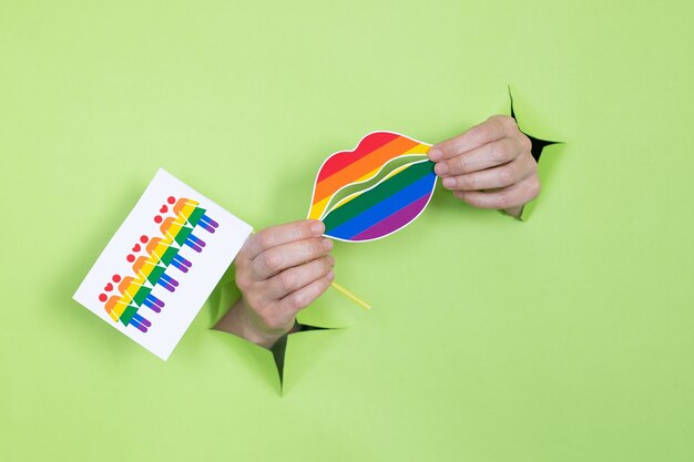 Foto vrouwelijke handen houden lippen en vlaggen vast in de kleuren van de regenboog op een groene achtergrond. lgbt-concept. plaats voor reclame.