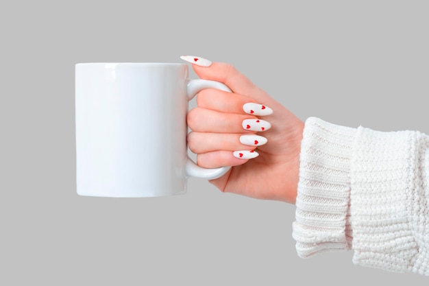 Vrouwelijke handen houden mock up witte lege mok op een grijze achtergrond cup voor Valentijnsdag manicure