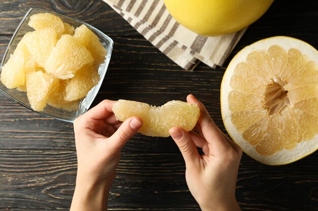 Vrouwelijke handen houden pomelo slice op houten tafel met rijpe pomelo