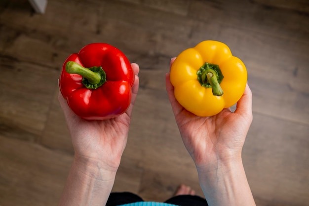 Vrouwelijke handen houden rode en gele paprika's vast op de achtergrond van een houten vloer Bovenaanzicht plat gelegd