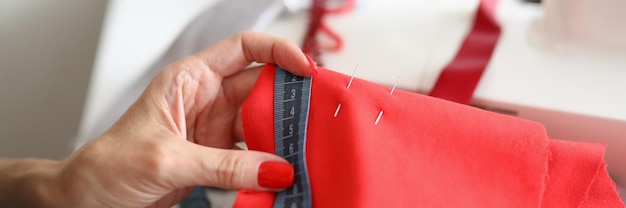 Vrouwelijke handen houden stof en een meetlint vast bij de naaimachine, de ontwerper van de naaister