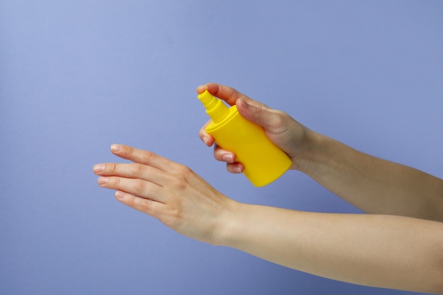 Vrouwelijke handen houden zonnebrandcrème op violette geïsoleerde achtergrond
