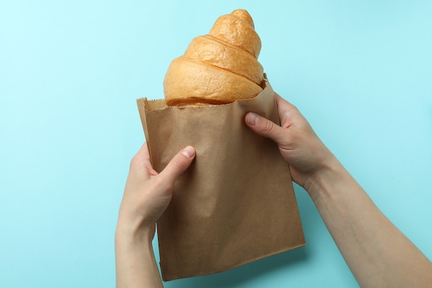 Vrouwelijke handen houdt papieren zak met croissant op blauw