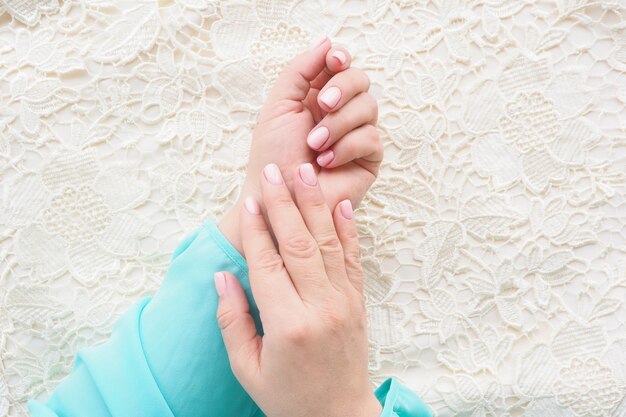 Vrouwelijke handen in een blauwe blouse met een mooie manicure en zacht roze nagellak op een beige kanten stof