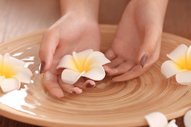 Vrouwelijke handen in een spa houten schaal met bloemen close-up