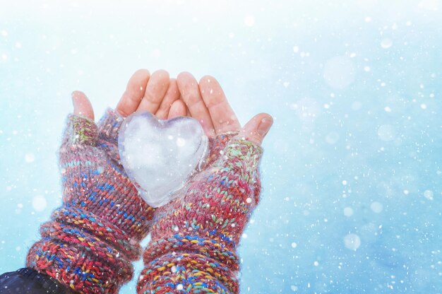 Vrouwelijke handen in gebreide handschoenen met een hart van ijs op een winterdag Liefde concept Valentijnsdag backgr