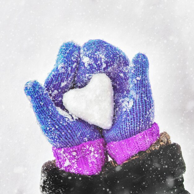 Vrouwelijke handen in gebreide handschoenen met een hart van sneeuw op een winterdag