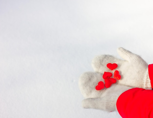 Vrouwelijke handen in gebreide witte wanten houden een zijden rood hart vast op een besneeuwde achtergrond