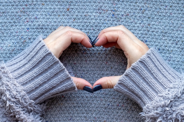 Foto vrouwelijke handen in trui met blauwe glinsterende nagels hartsymbool maken op gebreide muur