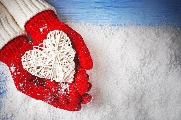 Vrouwelijke handen in wanten met decoratief hart op sneeuwachtergrond