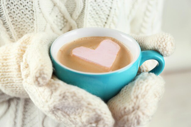 Vrouwelijke handen in warme wanten met kop warme cappuccino met hart marshmallow close-up