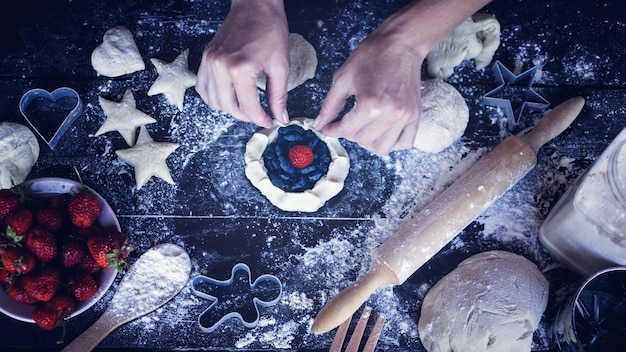 Vrouwelijke handen koken zelfgemaakte deeg cake met een vulling van rijpe aardbeien en sappige bessen van een kamperfoelie