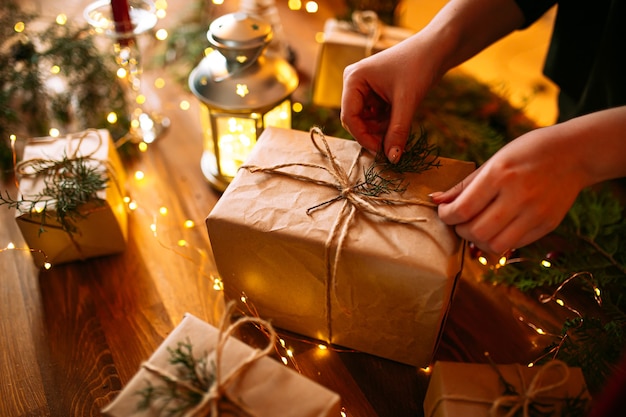 Vrouwelijke handen koppelverkoop vakantie ambachtelijke geschenkdoos met vuren takken op de houten tafel