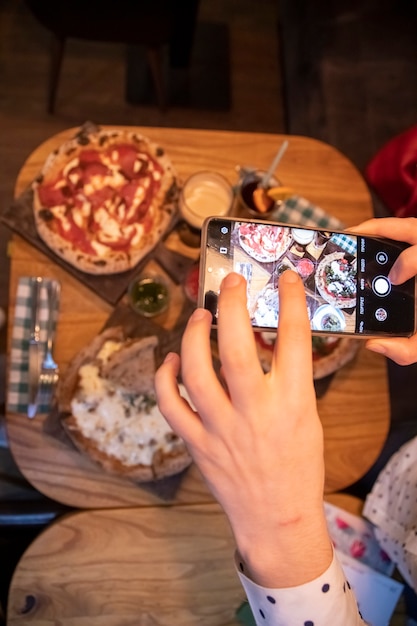 Vrouwelijke handen maakt foto's op een smartphonetafel met een heerlijke pizza in een restaurant. bovenaanzicht